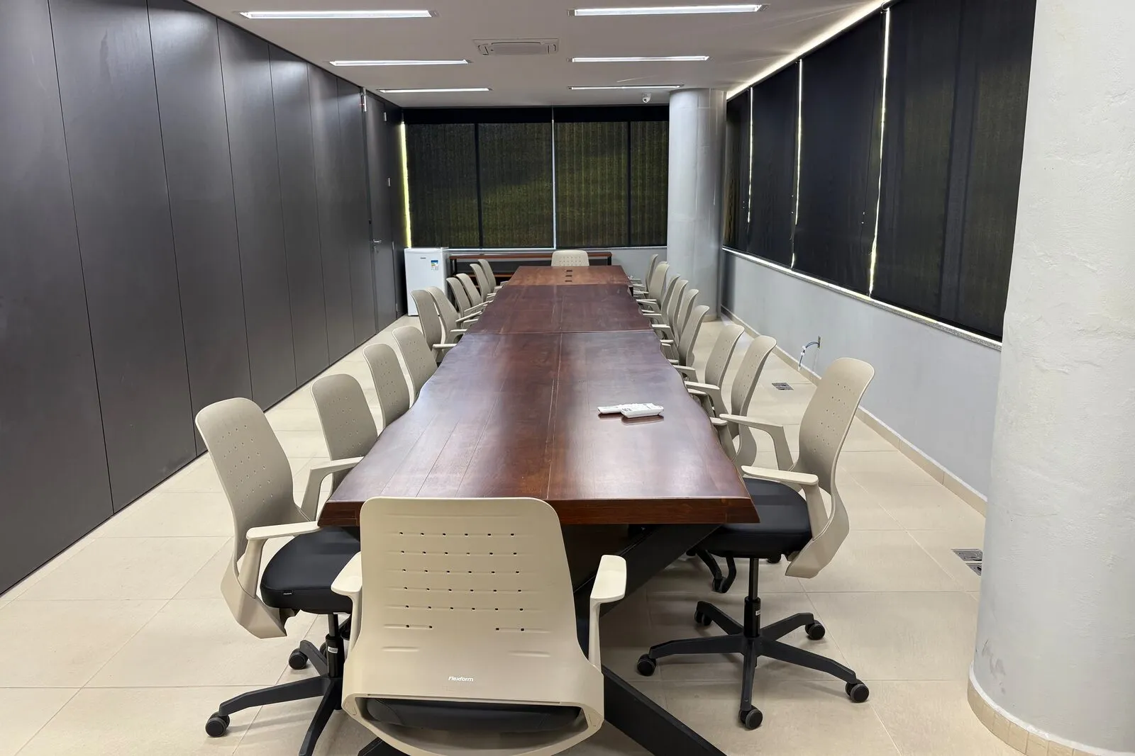 Sala de reuniões do Elume com mesa longa de madeira, cadeiras giratórias e persianas fechadas